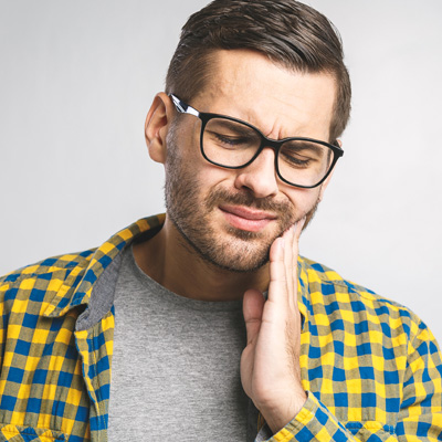 A man with glasses wearing a yellow plaid shirt and holding his hand to his mouth, possibly in pain or discomfort.