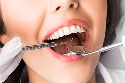 A person with a mouth open wide, holding dental instruments, possibly during a dental procedure.