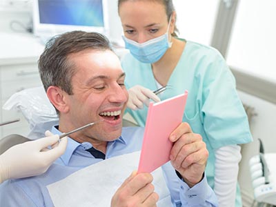 A man sitting in a dental chair with paperwork, being attended to by a dental professional who is showing him something on a tablet.