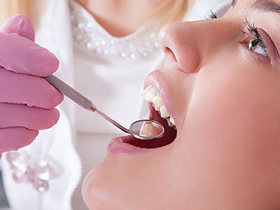 An adult woman with open mouth receiving dental treatment from a dental professional wearing gloves and using dental instruments.