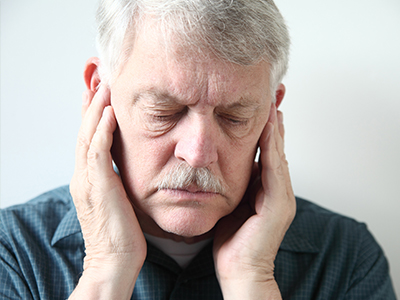 The image depicts an older man with his hand on his face, likely expressing pain or discomfort.