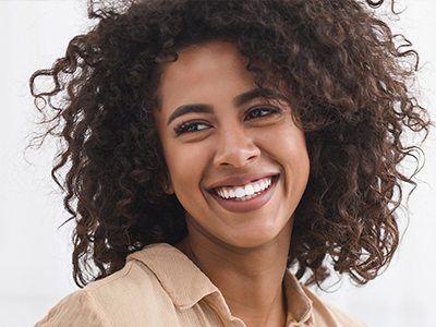 A woman with curly hair smiles broadly at the camera, against a neutral background.